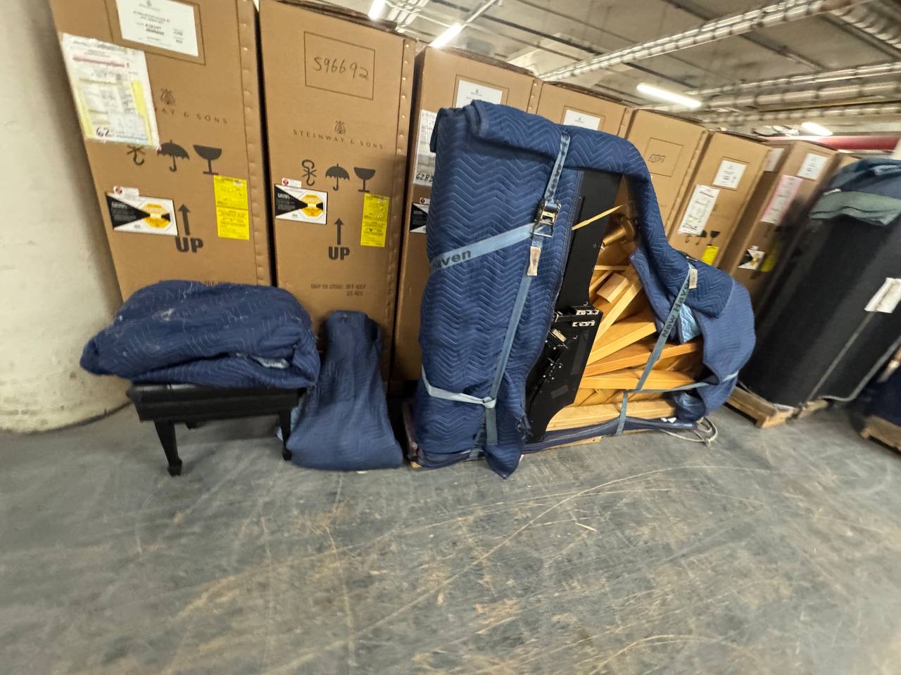 Grand piano on its side with moving blankets and securing straps